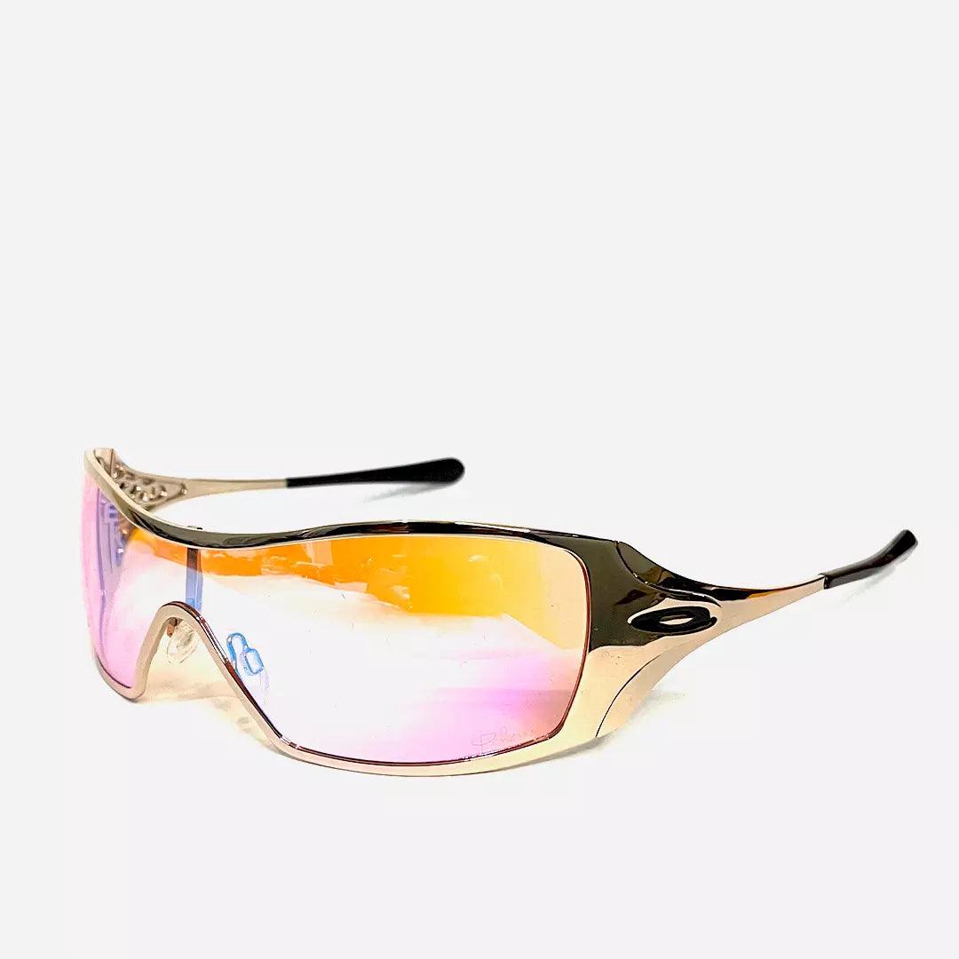 Óculos de sol Dynamic Rose Gold com lentes espelhadas em rosa e dourado, armação metálica dourada estilizada com detalhes curvados. Sofisticação e proteção em um design único.