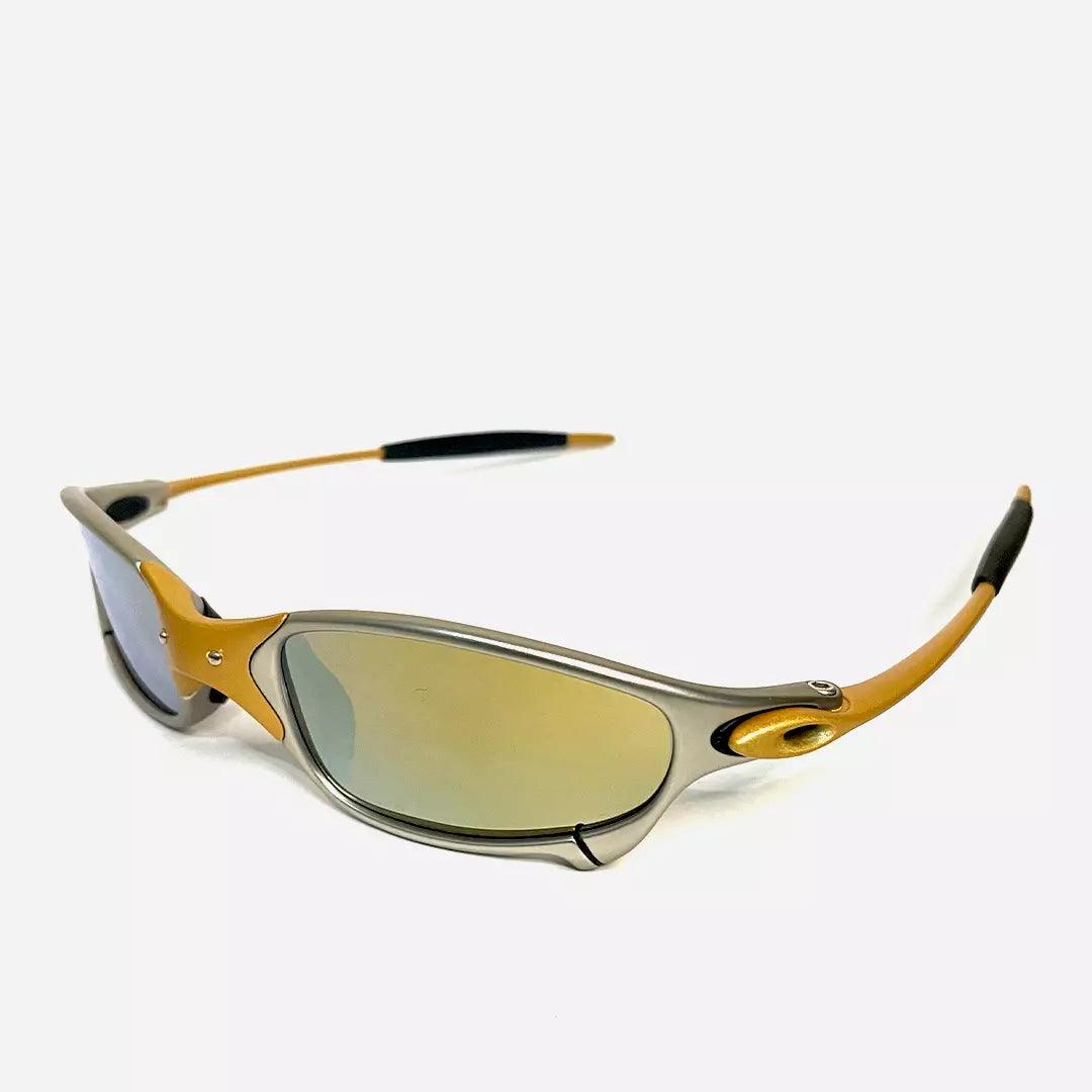 Óculos de sol Juliet com armação cinza e detalhes dourados, lentes espelhadas douradas, visto de ângulo lateral que destaca o design aerodinâmico e sofisticado. Modelo exclusivo da Lottus Unique, perfeito para um estilo esportivo e elegante.