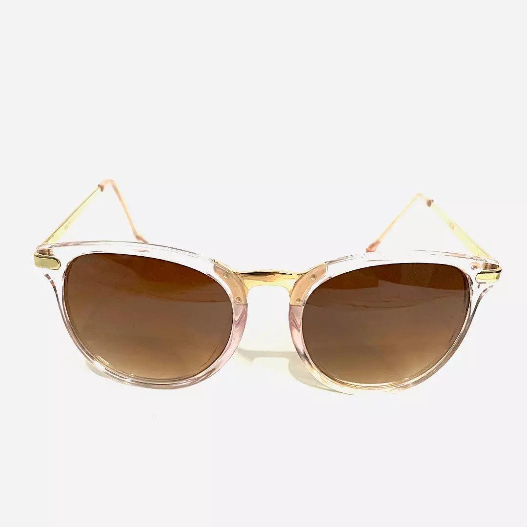 Óculos de sol Meteor Ray com design retrô, armação transparente rosada, detalhes em dourado e lentes marrons graduais, para um estilo sofisticado e atemporal.