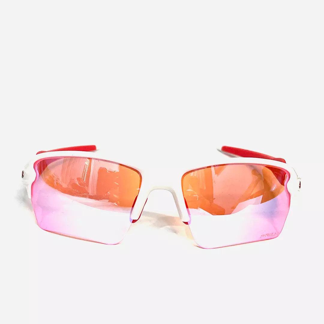 Óculos de sol Racer Rose White com lentes espelhadas em tom rosa e laranja, armação branca com detalhes em vermelho. Modelo esportivo para proteção UV e estilo.